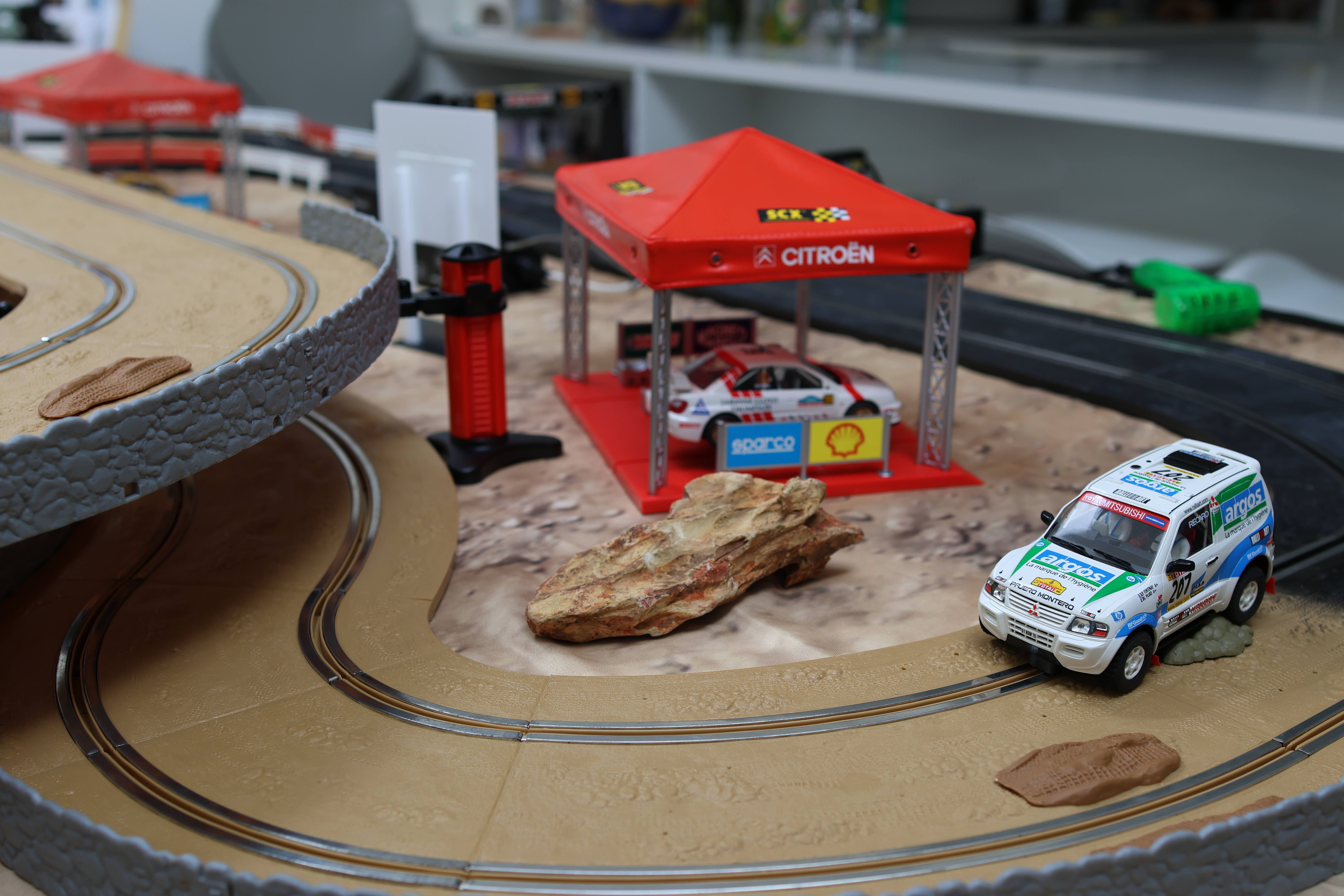 Off-road Scalextric track corner with rally car passing a desert rock and Citroen gazebo